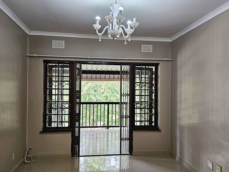 An empty living room featuring tiled flooring, security gates leading to a balcony, and neutral wall finishes, offering a blank canvas for personalization.