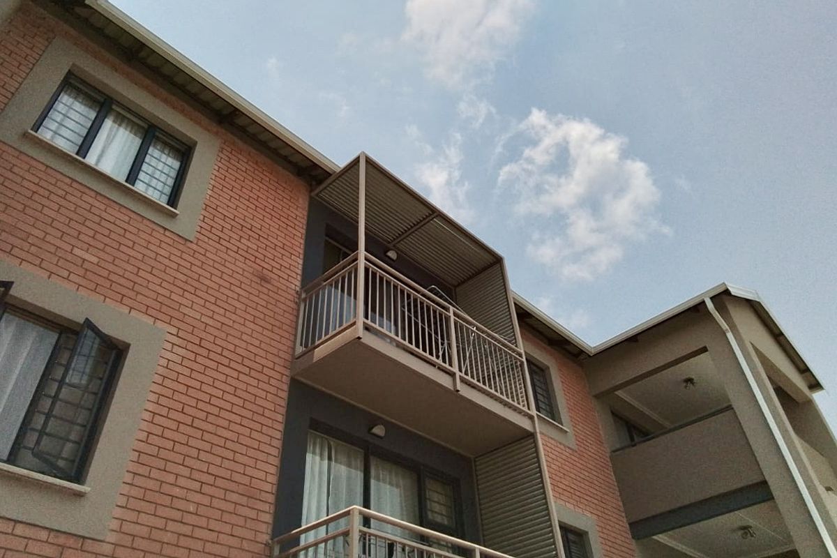 Exterior view of an apartment building featuring red brick facade, private balconies with metal railings, and sliding glass doors.