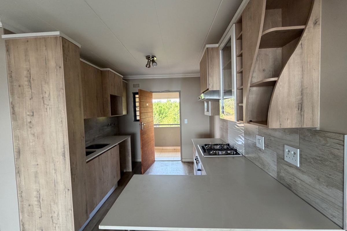 Modern kitchen featuring light wood-look cabinetry, stone countertops, a gas hob, and an integrated extractor fan, leading out to a balcony.