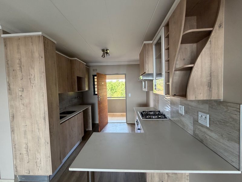 Modern kitchen featuring light wood-look cabinetry, stone countertops, a gas hob, and an integrated extractor fan, leading out to a balcony.