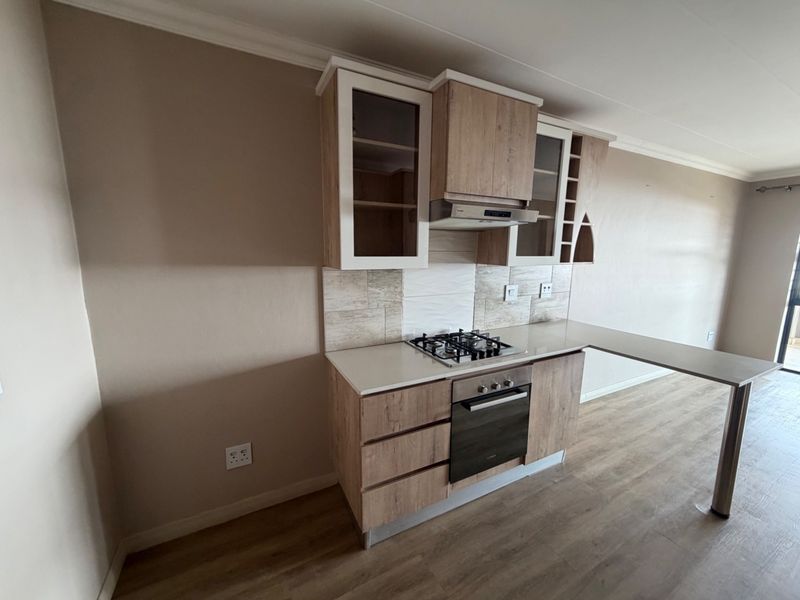 Modern kitchen featuring wood-finish cabinetry, stone countertops, a gas hob, built-in oven, extractor fan, and an integrated breakfast bar.