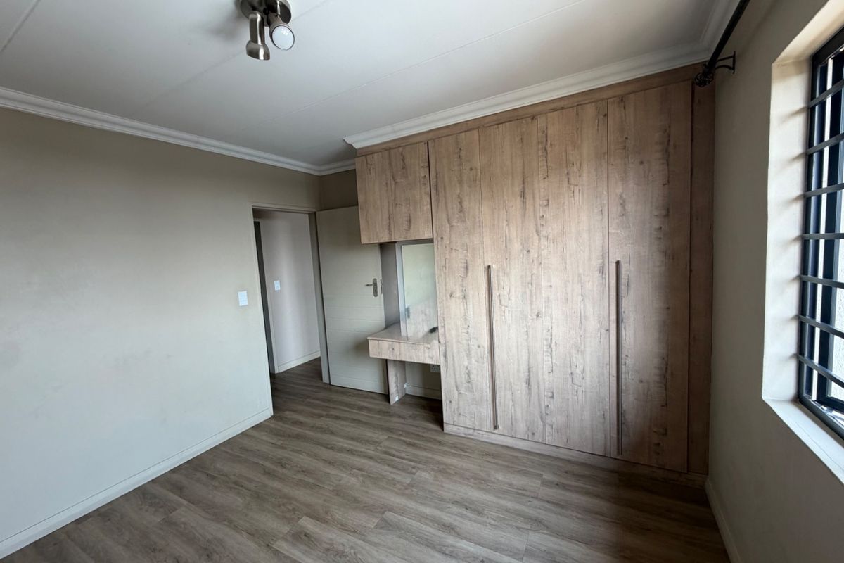 A clean, empty bedroom featuring modern wood-look laminate flooring, built-in cupboards with an integrated vanity, and a ceiling light fixture.