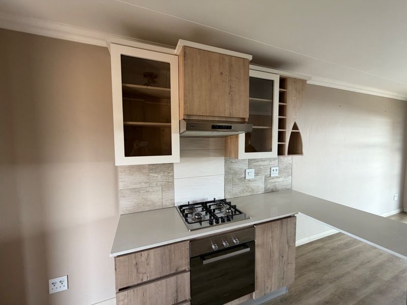 Modern kitchen featuring wood-finish cabinetry, stone countertops, a built-in gas hob, oven, and extractor fan with a stylish tiled backsplash.