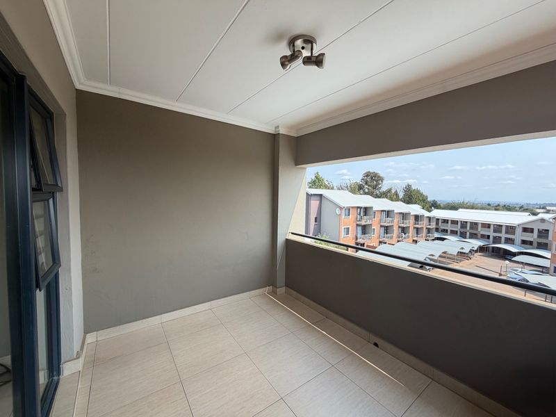 A clean, covered balcony featuring tiled flooring, a metal balustrade, and a ceiling light fixture, offering an open view of the complex.