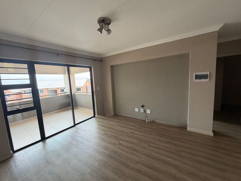 An empty living room featuring laminate flooring, a sliding glass door leading to a balcony, and a neutral wall finish.
