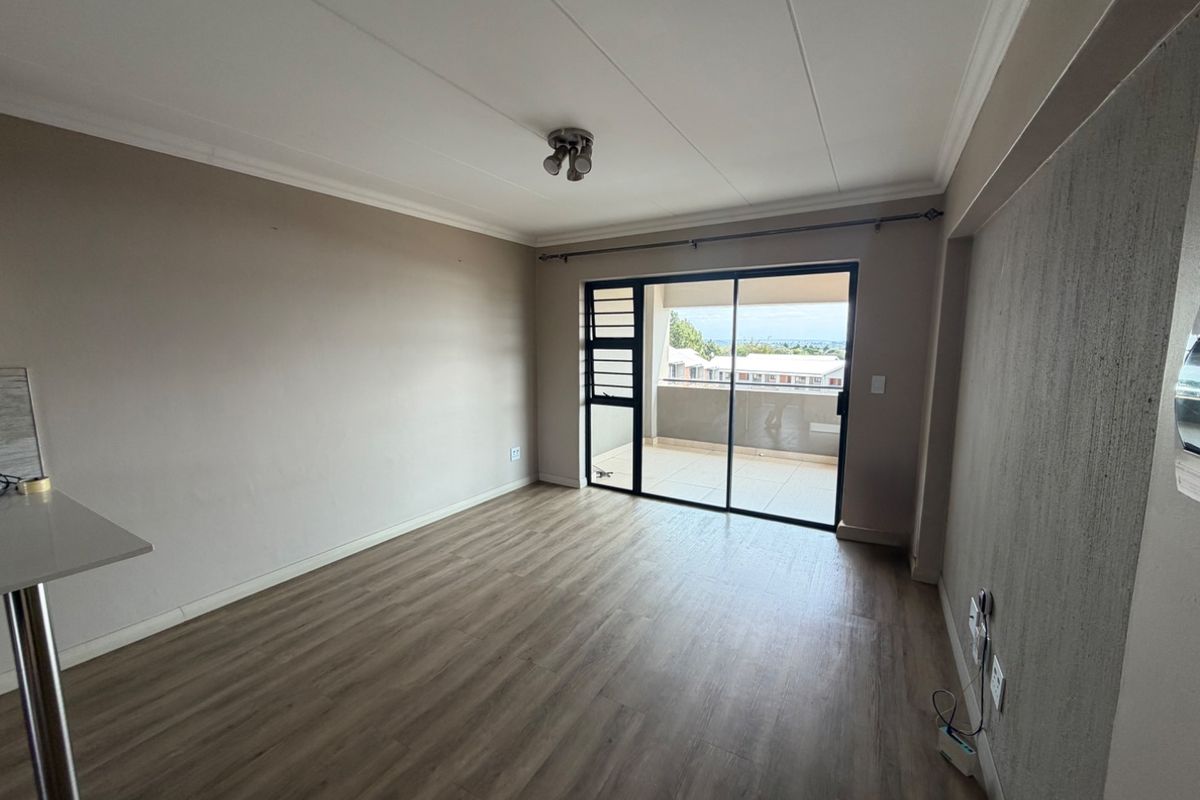 A bright, empty living room featuring modern laminate flooring, a textured accent wall, and a sliding glass door leading to a private balcony.