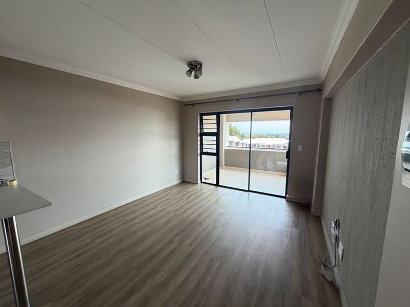 A bright, empty living room featuring modern laminate flooring, a textured accent wall, and a sliding glass door leading to a private balcony.