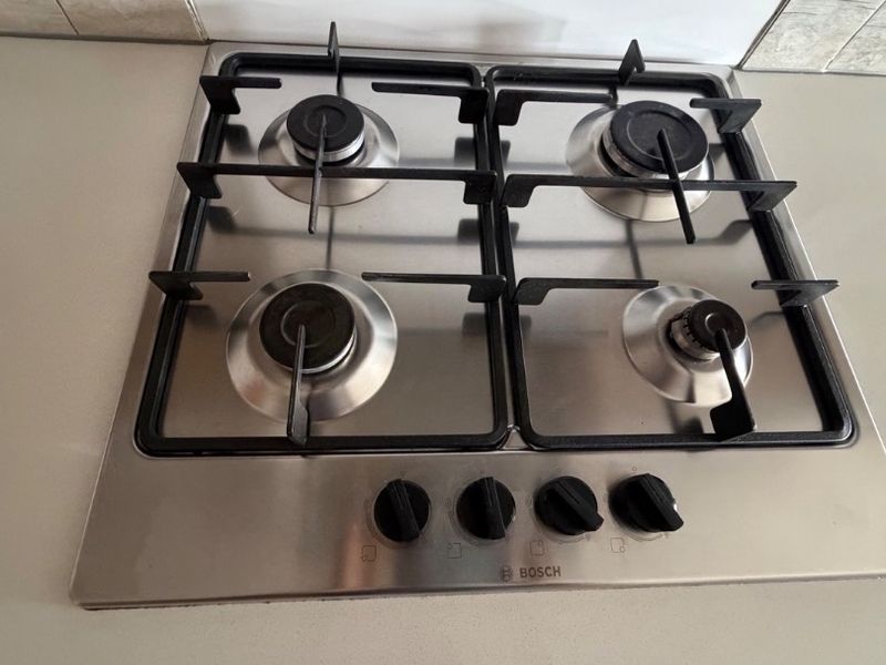 A clean, stainless steel Bosch four-burner gas cooktop integrated into a stone countertop with a modern tiled backsplash.