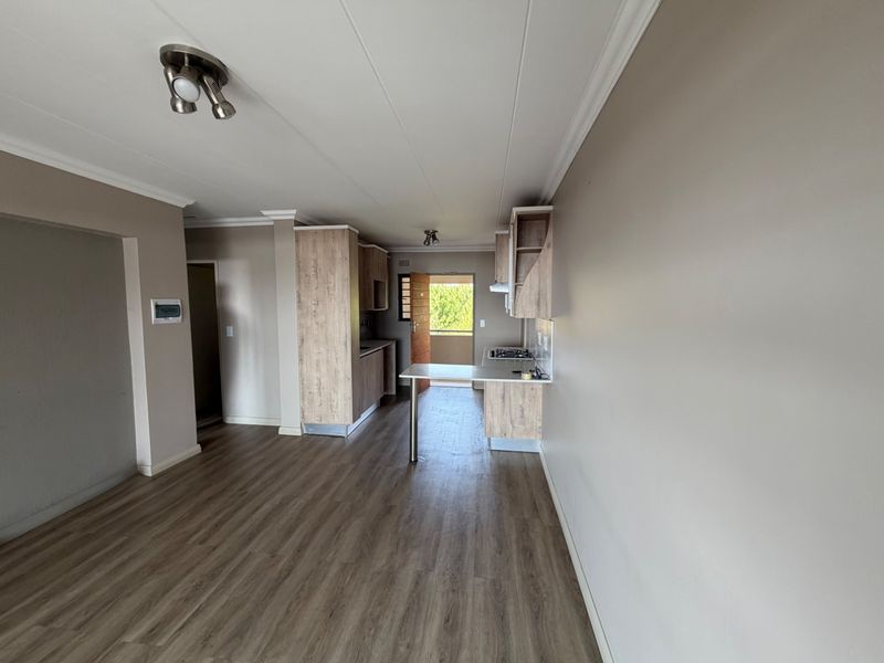 An open-plan living and kitchen area featuring modern laminate flooring, neutral walls, and a functional kitchen with built-in cabinetry and a breakfast bar.