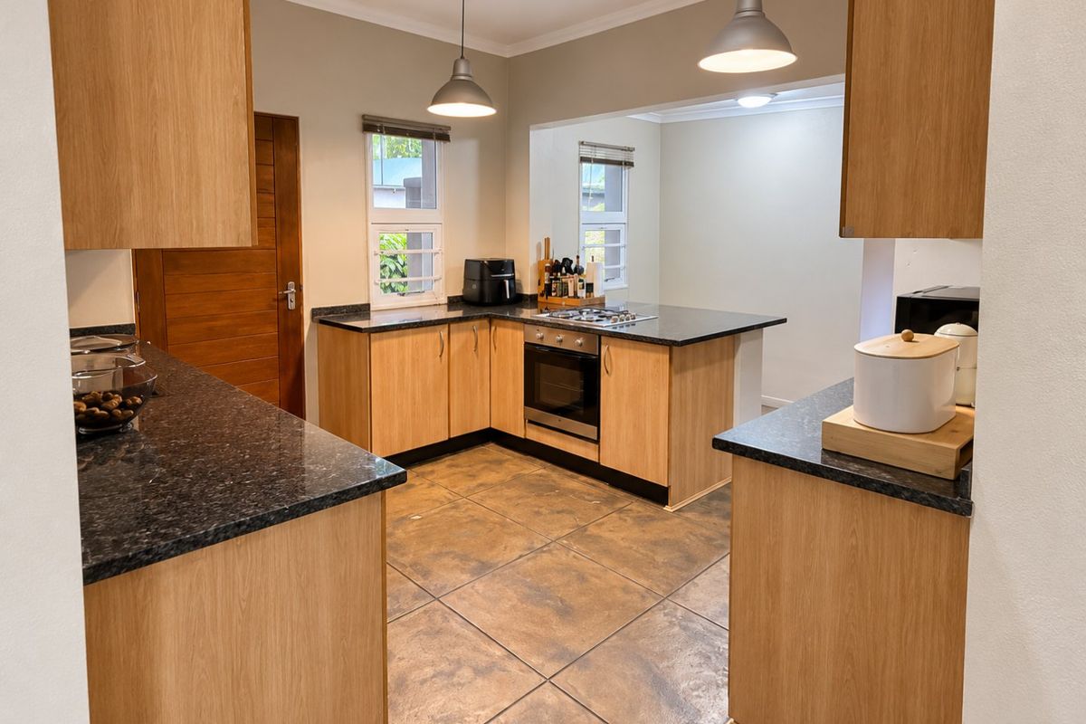 A well-maintained kitchen featuring light wood cabinetry, dark granite countertops, built-in oven, gas hob, and tiled flooring with modern pendant lighting.