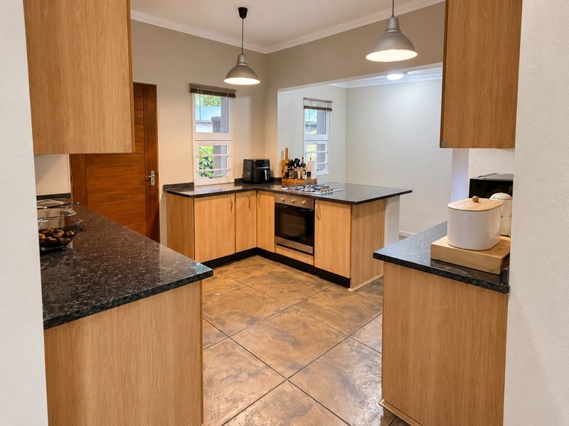 A well-maintained kitchen featuring light wood cabinetry, dark granite countertops, built-in oven, gas hob, and tiled flooring with modern pendant lighting.