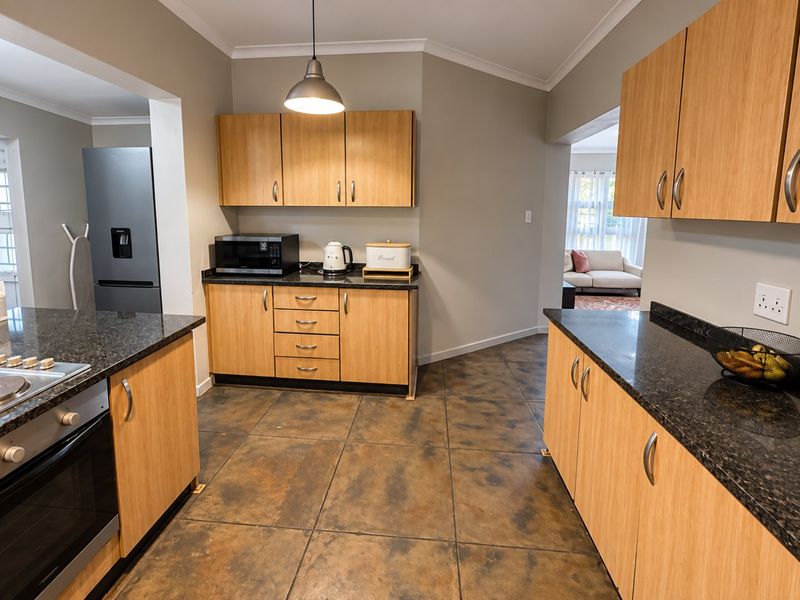 A functional kitchen featuring light wood cabinetry, dark granite countertops, built-in oven, hob, and tiled flooring with an open-plan layout.