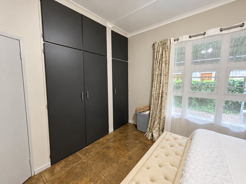 A well-maintained bedroom featuring dark built-in cupboards, tiled flooring, and a large window allowing for natural light.