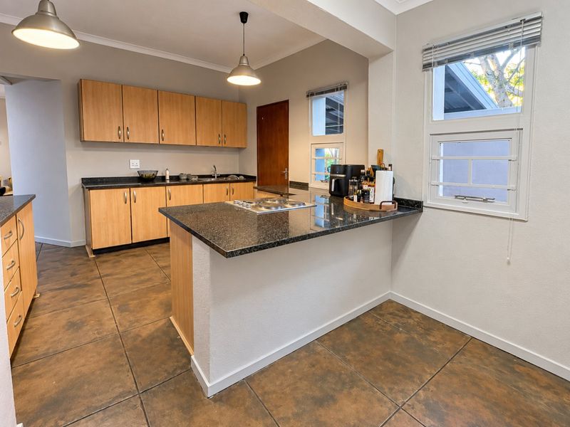 A functional kitchen featuring light wood cabinetry, dark granite countertops, a built-in hob, and tiled flooring with ample natural light.