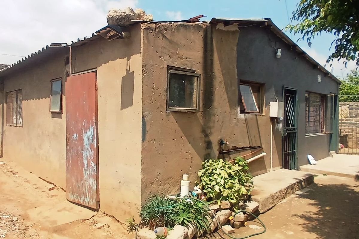 Exterior view of a single-story dwelling showing significant wear to the exterior plaster, roof structure, and door finishes.