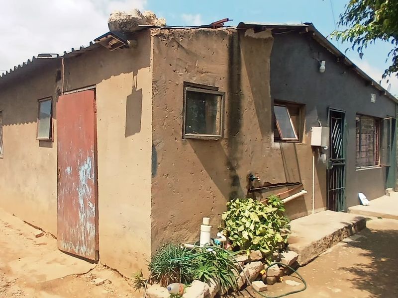 Exterior view of a single-story dwelling showing significant wear to the exterior plaster, roof structure, and door finishes.