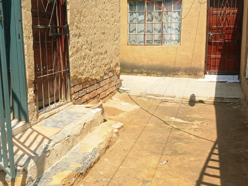 A rear exterior view of the property showing a small courtyard area with security gates and weathered brick and plastered wall finishes.