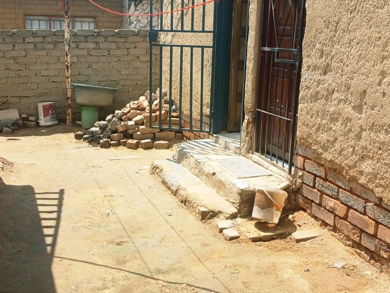 A rear exterior area featuring a security gate, concrete steps, and exposed brick walls, requiring maintenance and landscaping to improve the property's outdoor space.