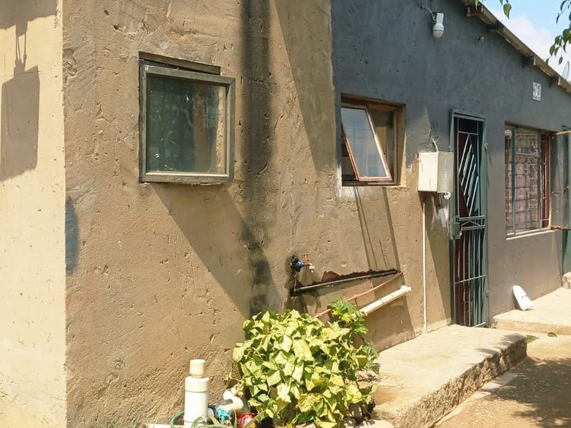 Rear exterior view of the property showing a concrete facade, security gate, and external plumbing fixtures in need of maintenance and cosmetic repair.