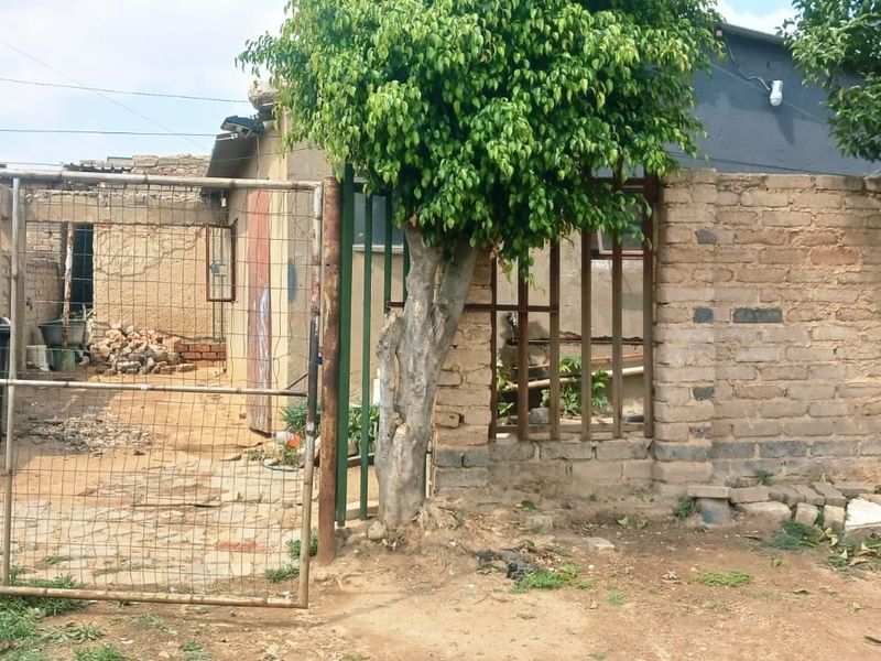 Front exterior view of the property featuring a brick boundary wall, metal gate, and unpaved yard area.