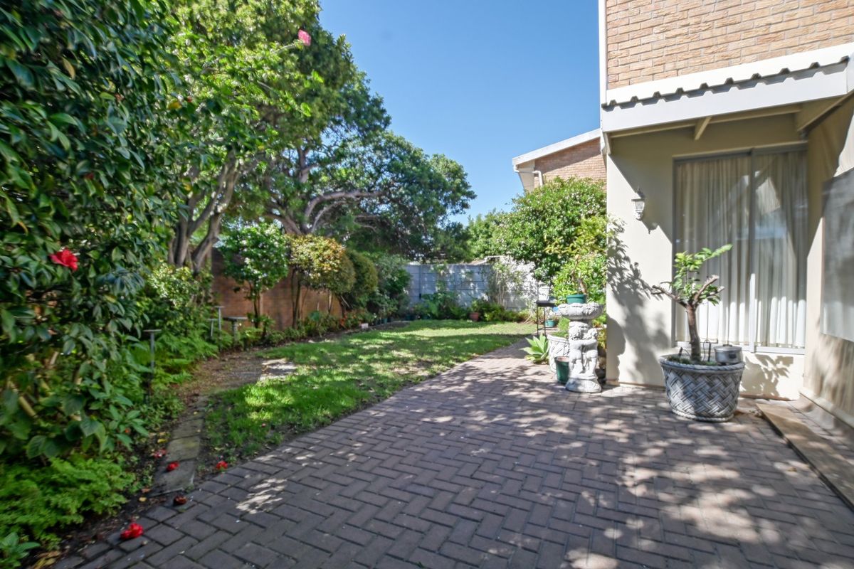 A private rear garden featuring a brick-paved patio area, established lawn, and mature perimeter landscaping, providing a peaceful outdoor space.
