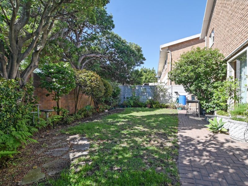 A private rear garden featuring a brick-paved patio area, established trees, and a lawn enclosed by boundary walls.