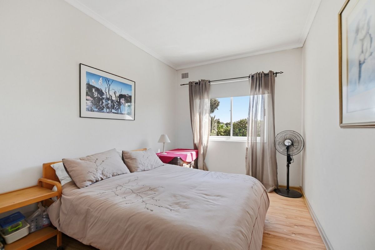 A functional bedroom featuring light-toned laminate flooring, neutral walls, and a sliding window that provides natural light and ventilation.