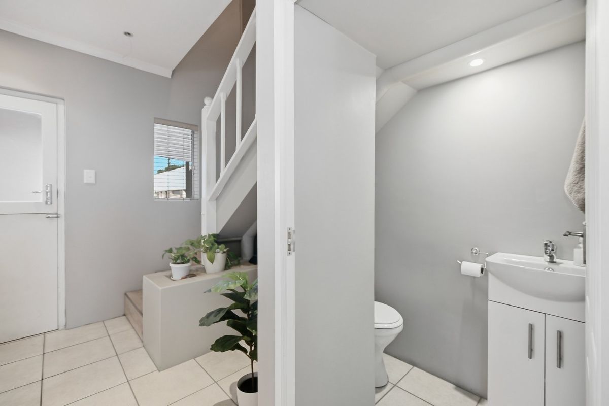 A compact guest bathroom featuring a modern vanity and toilet, situated conveniently beneath a staircase with tiled flooring and neutral finishes.