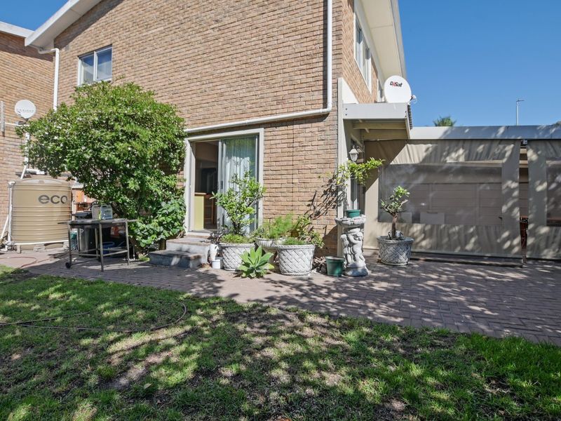 Rear exterior view of the property featuring a brick facade, paved patio area, and an enclosed outdoor space with a water tank.