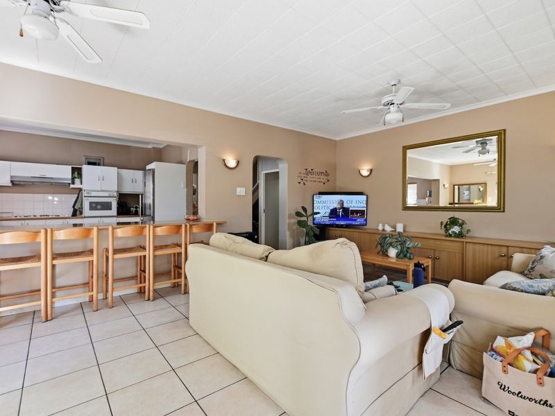 Open-plan living and kitchen area featuring tiled floors, ceiling fans, and a functional kitchen layout with built-in cabinetry and breakfast bar seating.