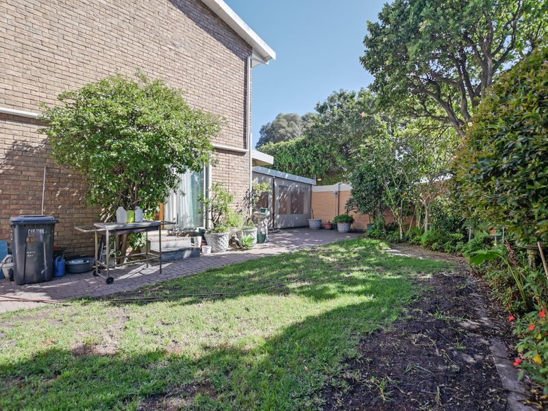 A private rear garden featuring a paved patio area, established greenery, and a brick exterior facade with a sliding door access.