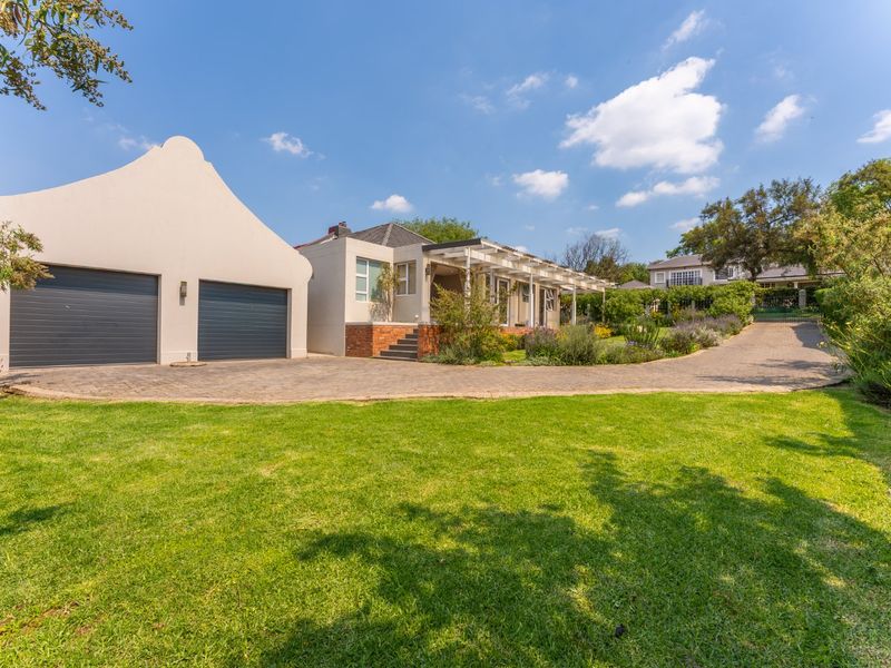 Front view of the property featuring a double garage, paved driveway, and a covered pergola entrance set within a well-maintained garden.