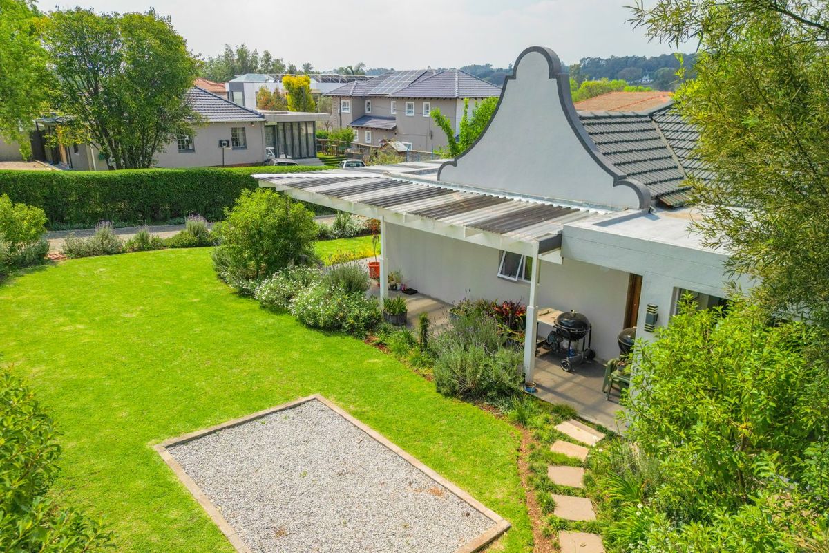 An elevated view of the rear exterior featuring a well-maintained garden, a gravel area, and a covered patio attached to the gabled house structure.