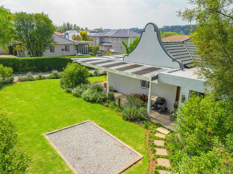 An elevated view of the rear exterior featuring a well-maintained garden, a gravel area, and a covered patio attached to the gabled house structure.
