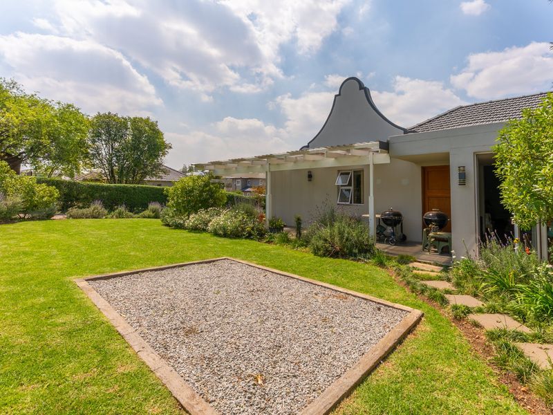 Rear view of the property featuring a landscaped garden, a gravel feature area, a covered pergola patio, and a classic gabled architectural design.
