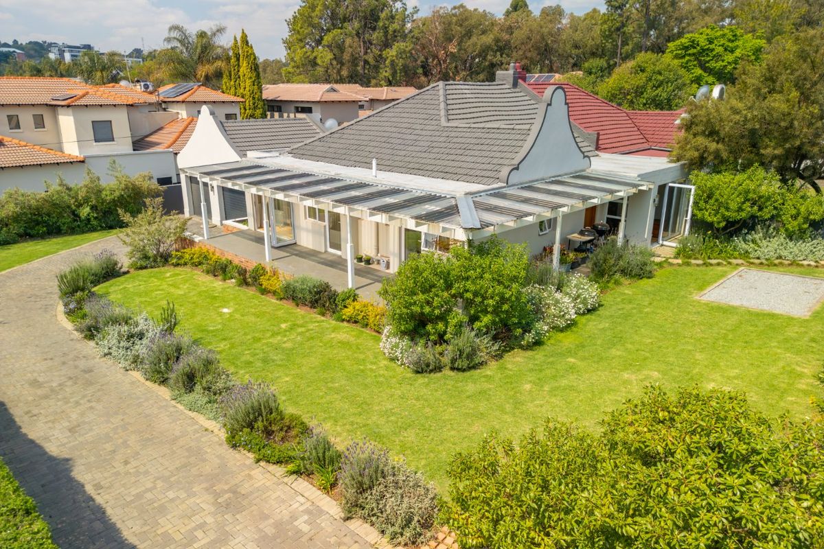 Aerial view of a well-maintained residential property featuring a gabled roof, a spacious covered patio, and a landscaped garden with a paved driveway.