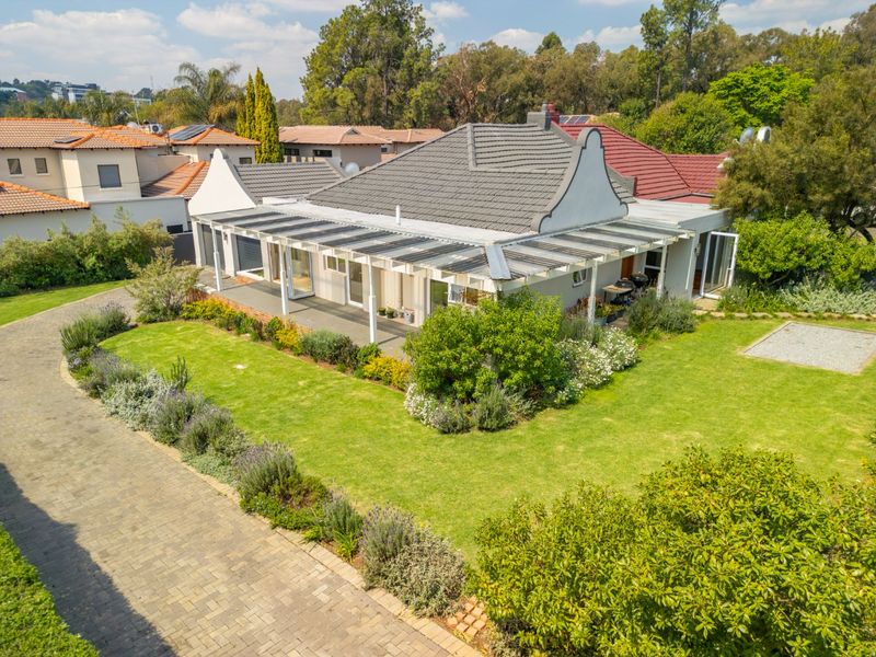 Aerial view of a well-maintained residential property featuring a gabled roof, a spacious covered patio, and a landscaped garden with a paved driveway.