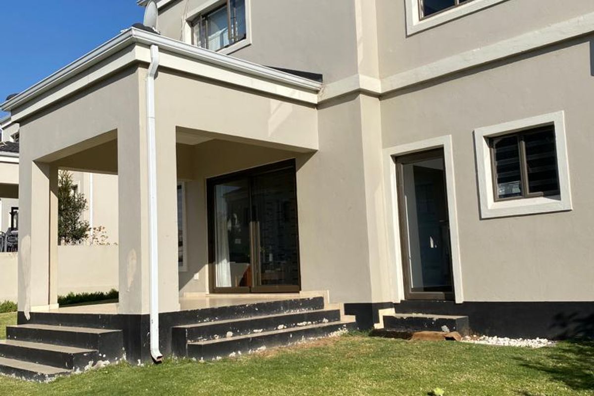 Rear view of a double-storey townhouse featuring a covered patio, sliding glass doors, and a small private garden area.