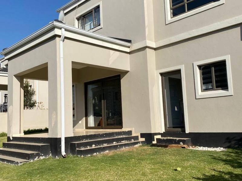 Rear view of a double-storey townhouse featuring a covered patio, sliding glass doors, and a small private garden area.