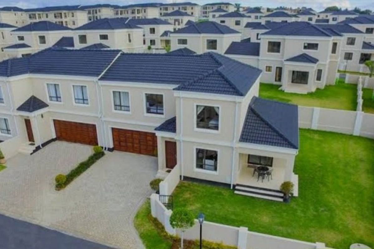 Aerial view of a modern townhouse complex featuring tiled roofs, paved driveways, private gardens, and secure boundary walls.