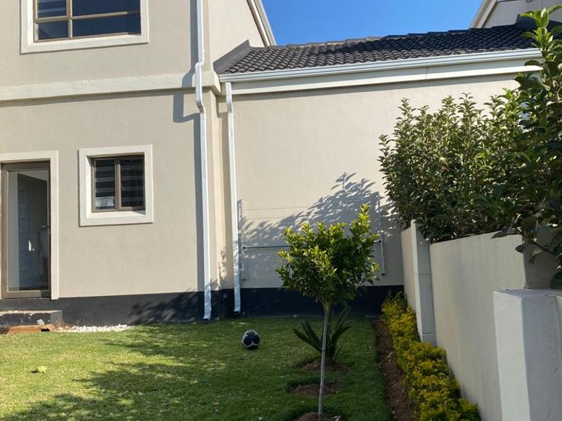 A well-maintained rear exterior view of the townhouse featuring a private garden, plastered walls, and established boundary landscaping.