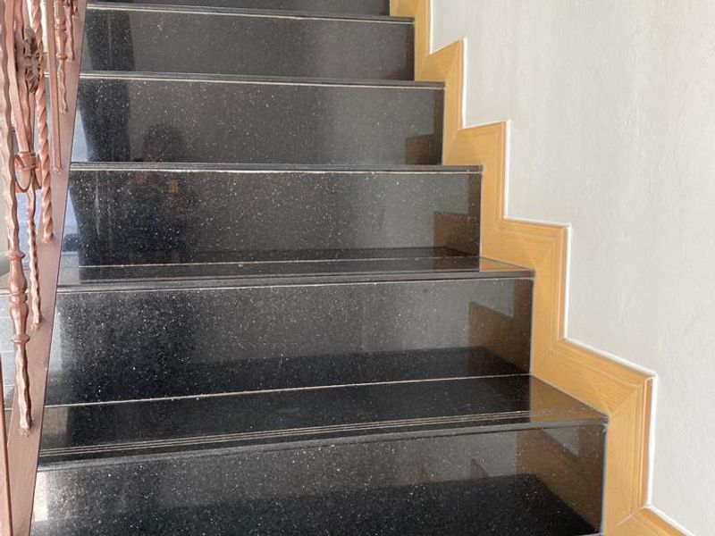 A staircase featuring polished black granite steps, a decorative wrought iron balustrade, and clean wooden skirting along the wall.