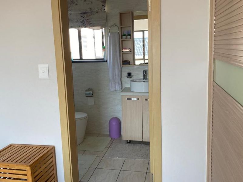 A view into a functional bathroom featuring a vessel sink vanity, tiled flooring, and a toilet, accessed through a wooden door frame.