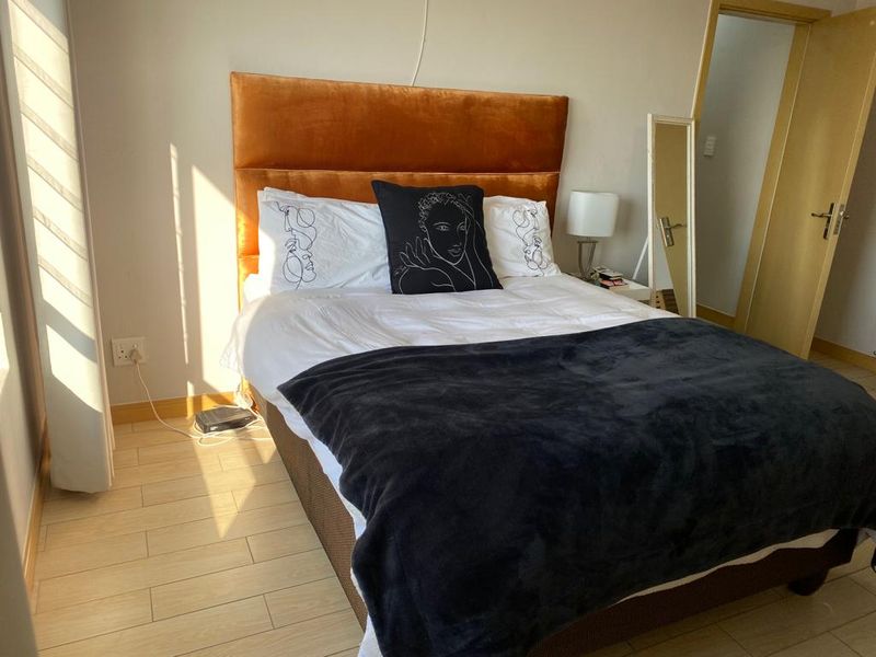 A well-lit bedroom featuring light-toned laminate flooring, neutral walls, and a standard internal door.