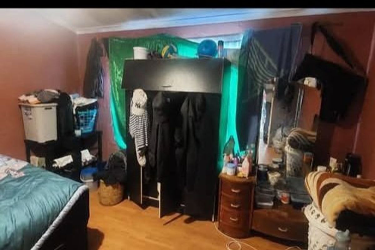 A bedroom featuring laminate flooring and a built-in wardrobe, currently cluttered with personal belongings.