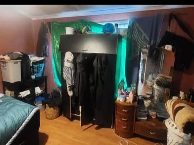 A bedroom featuring laminate flooring and a built-in wardrobe, currently cluttered with personal belongings.