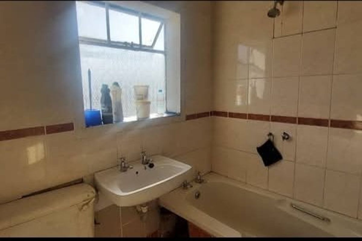 A dated bathroom featuring ceramic wall tiles, a pedestal washbasin, and a standard bathtub with a shower head.