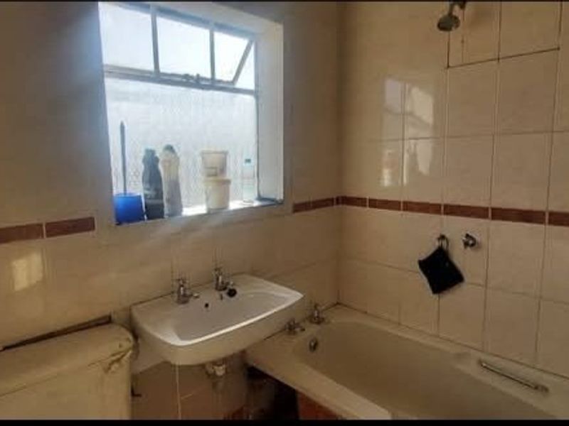A dated bathroom featuring ceramic wall tiles, a pedestal washbasin, and a standard bathtub with a shower head.