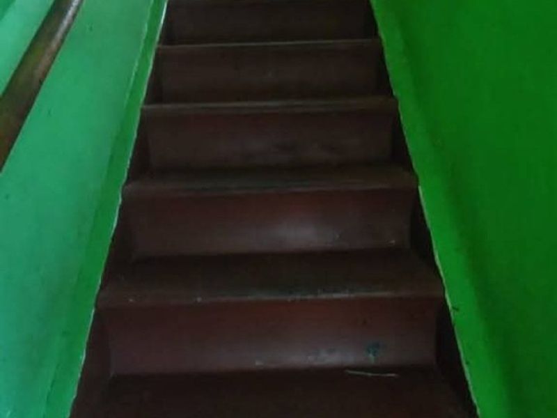 A narrow interior staircase featuring a wooden handrail and painted steps, providing access between levels.