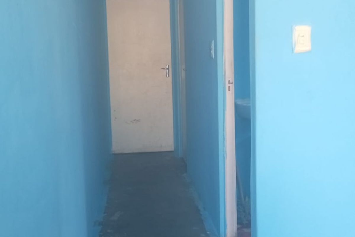 A narrow interior hallway featuring blue painted walls, a ceiling light fixture, and access to adjacent rooms.